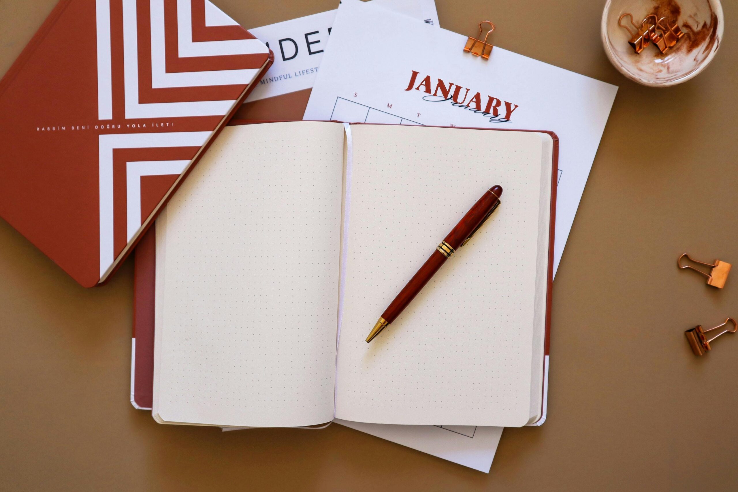 Flat lay of an open notebook with a pen, surrounded by a January calendar and stationery items.